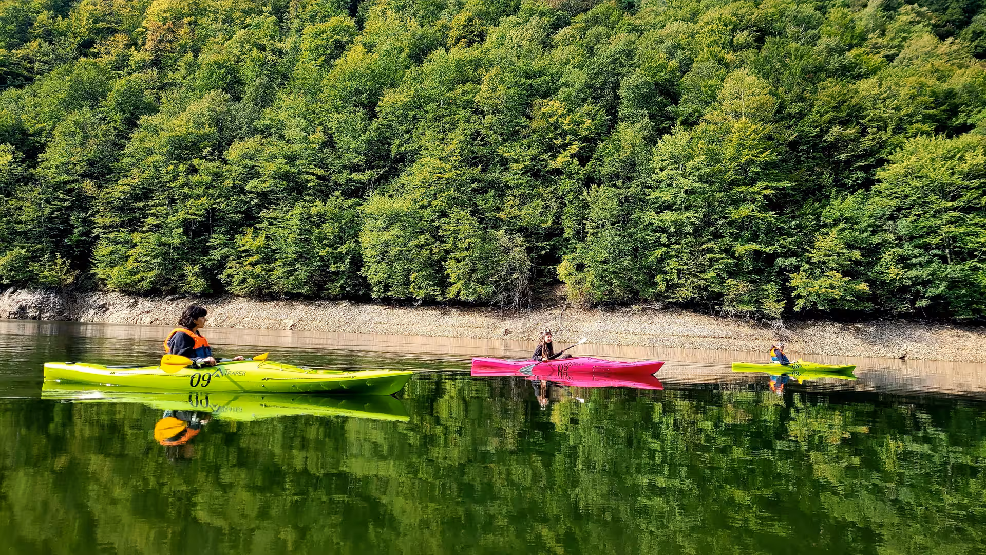 Three kayakers paddling colorful kayaks on a calm lake surrounded by lush Carpathian mountain forest