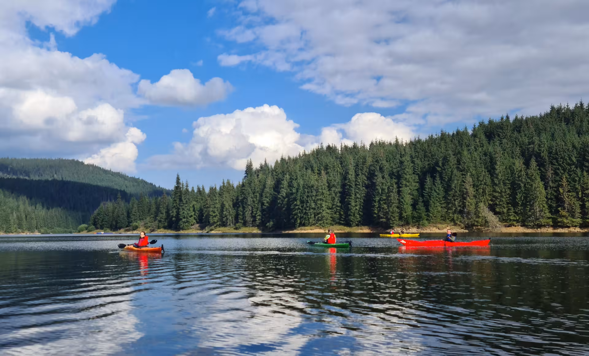 Kayakers paddling colorful kayaks on a calm mountain lake surrounded by dense pine forests in the Carpathians