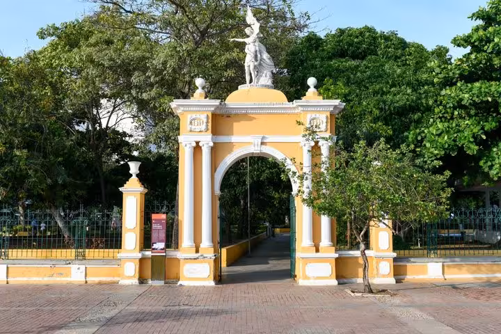 Yellow colonial arch gate entrance to Cartagena park with white statue on top