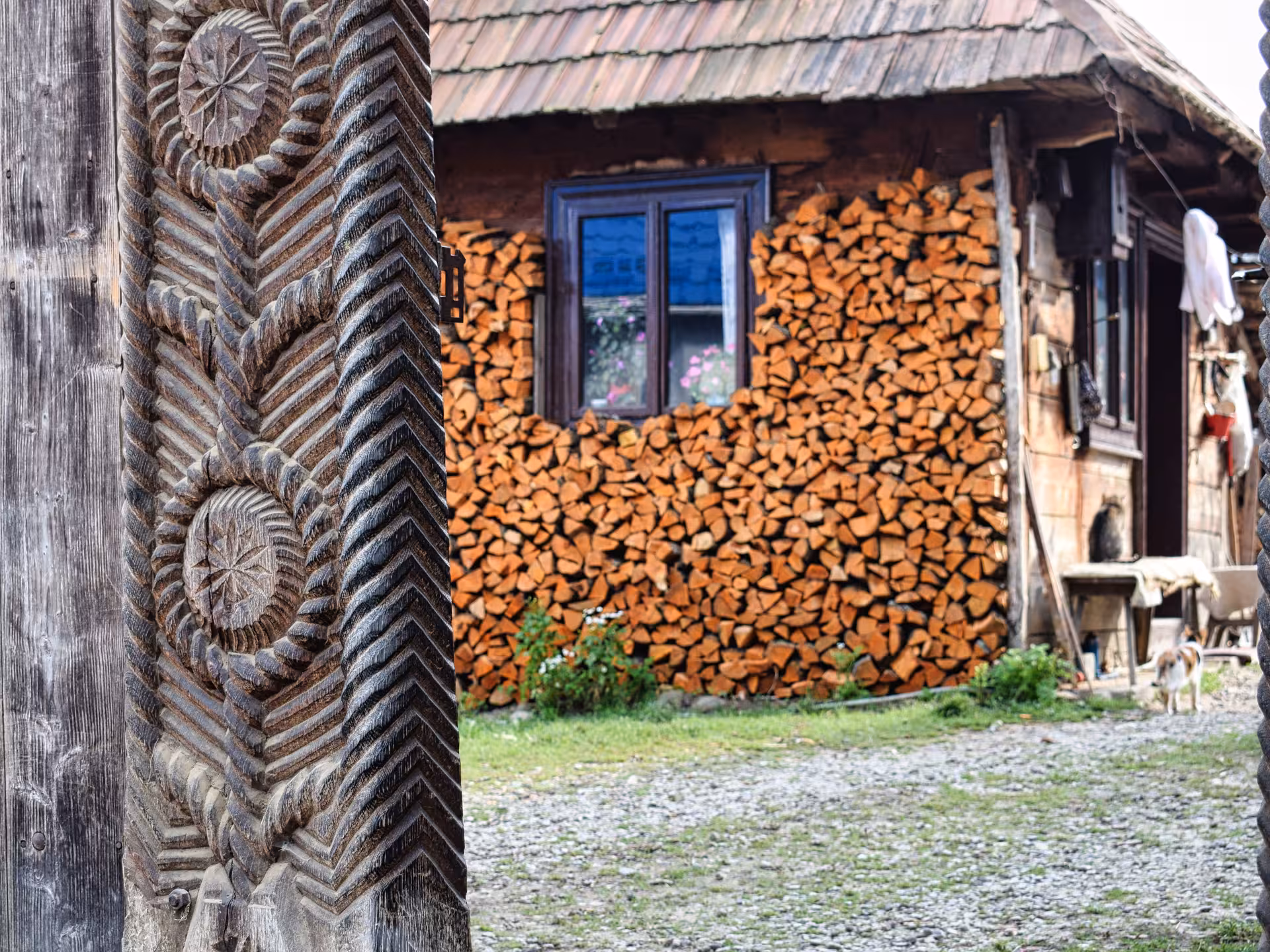 Detailed carved wooden gate pillar with stacked firewood and rustic Maramures farmhouse on a 3-day tour from Cluj