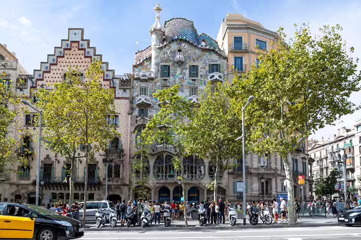 Street view of Casa Batlló and neighboring modernist buildings on Passeig de Gràcia, with tourists queuing for morning entry