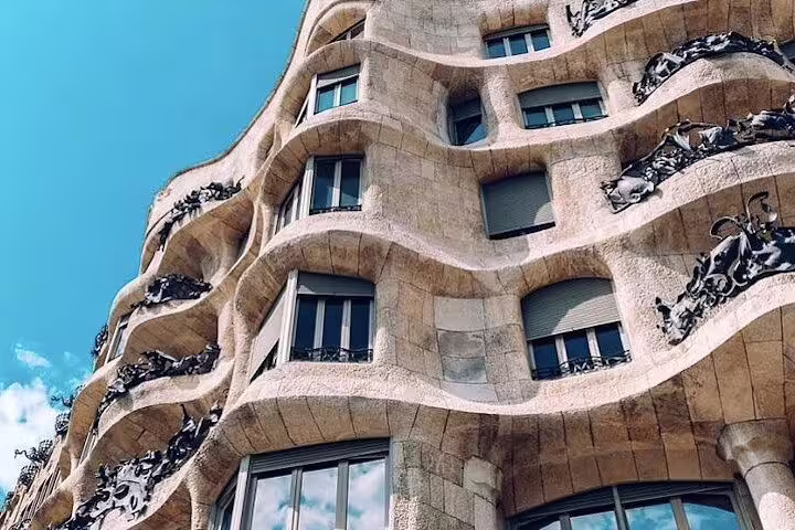 Close-up of the wavy, stone facade of Casa Milà in Barcelona, showcasing its unique architectural design under a vibrant blue sky.