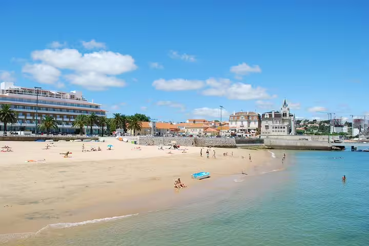 Sunny beach scene in Cascais with people enjoying the sandy shore and clear blue waters, perfect for a panoramic tour.
