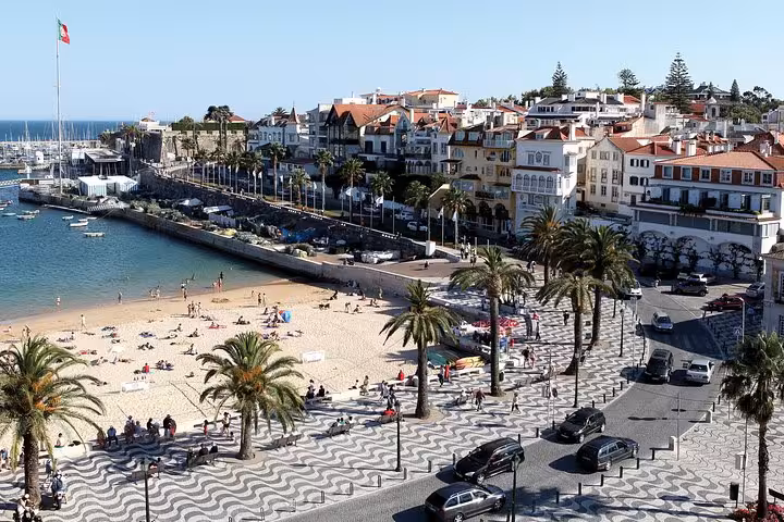 Bright beach scene in Cascais with sandy shores, palm trees, and vibrant architecture, ideal for a private tour stop.