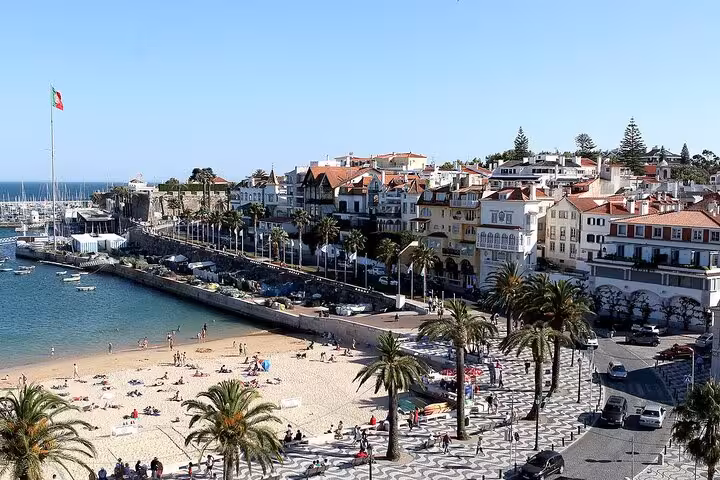 Bustling Cascais beach and promenade with charming architecture and palm trees under a clear blue sky.