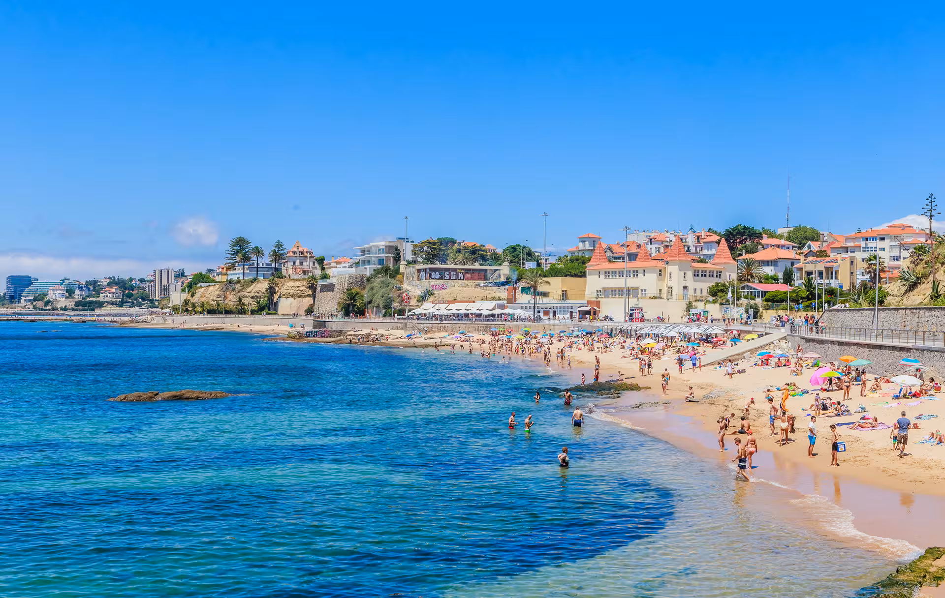 Scenic view of Cascais beach with vibrant umbrellas and people enjoying the sun, ideal for a Lisbon day trip.