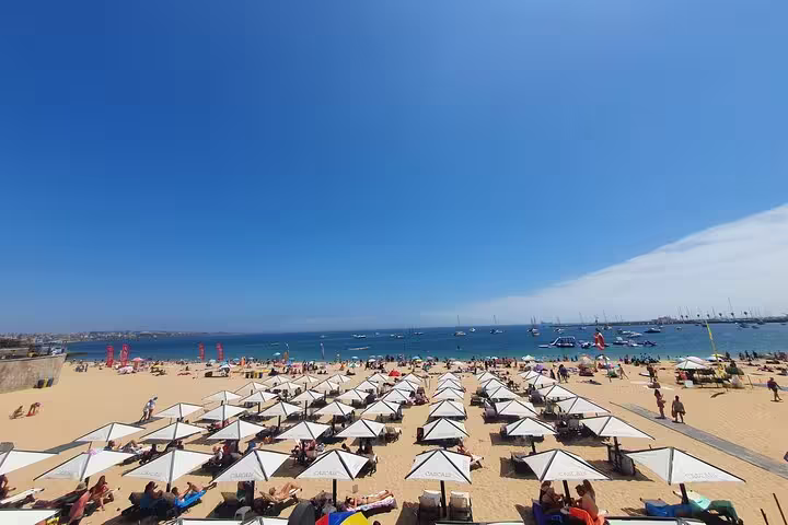 Sunny day at Cascais beach with rows of umbrellas and beachgoers enjoying the ocean view, featured on the small-group tour.