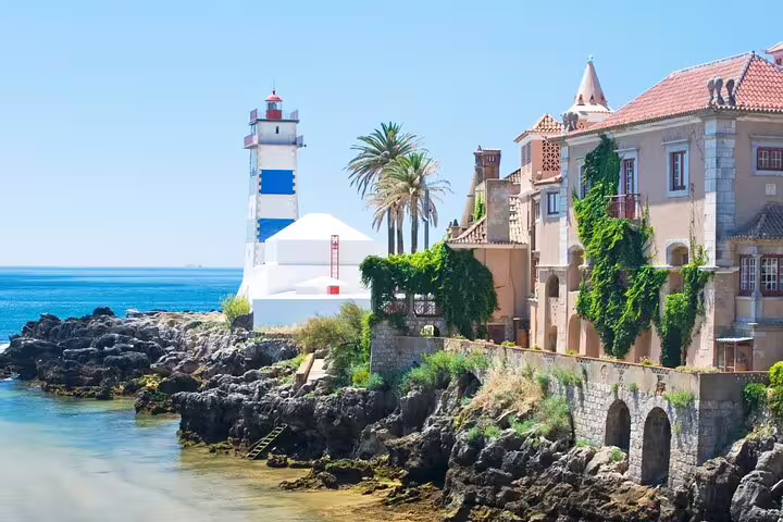 Scenic view of Cascais coastline with historic buildings and iconic lighthouse, featured in our full-day Sintra tour.