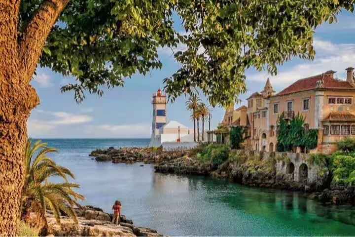 Scenic view of Cascais coastline with historic buildings and lighthouse, perfect for Sintra and Cascais full-day tour experience.