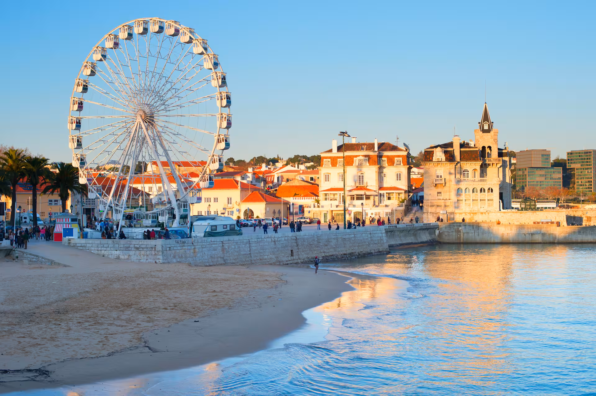 Scenic view of Cascais beachfront with Ferris wheel and historic architecture at sunset, perfect for beach tours.
