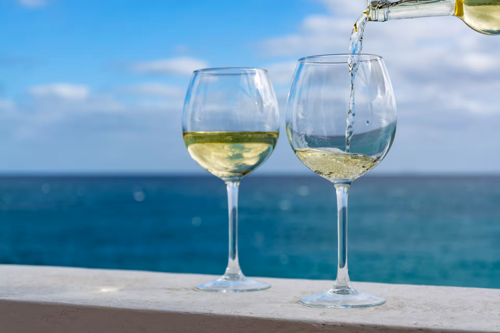 Refreshing white wine being poured into glasses with a stunning ocean view in the background in Cascais.