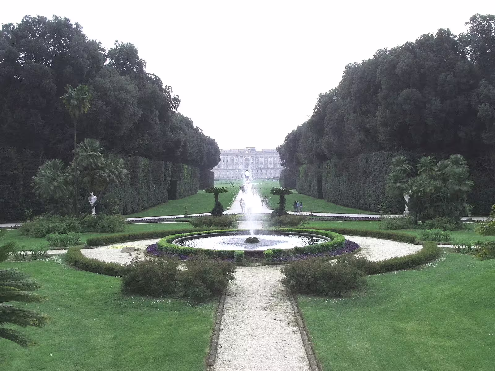 Panoramic view of the formal gardens and central fountain leading to the majestic Royal Palace of Caserta in Campania