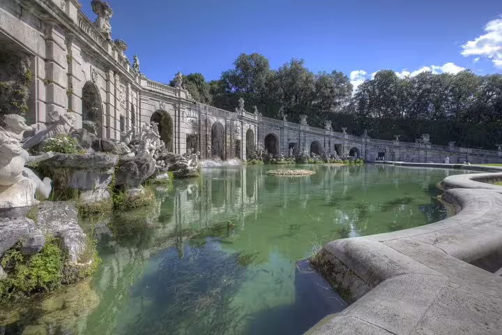 Ornate marble statues and reflective pool in the landscaped gardens of the Royal Palace of Caserta on a guided tour