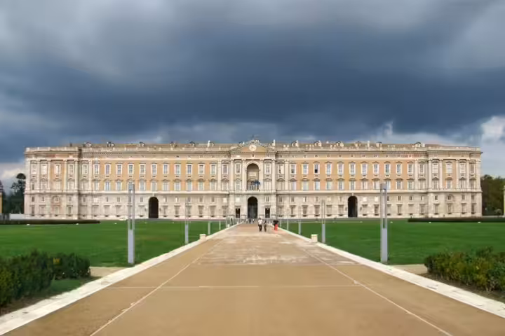 Front view of Caserta Royal Palace with grand façade, wide pathway and green lawn on a private transfer day trip from Naples
