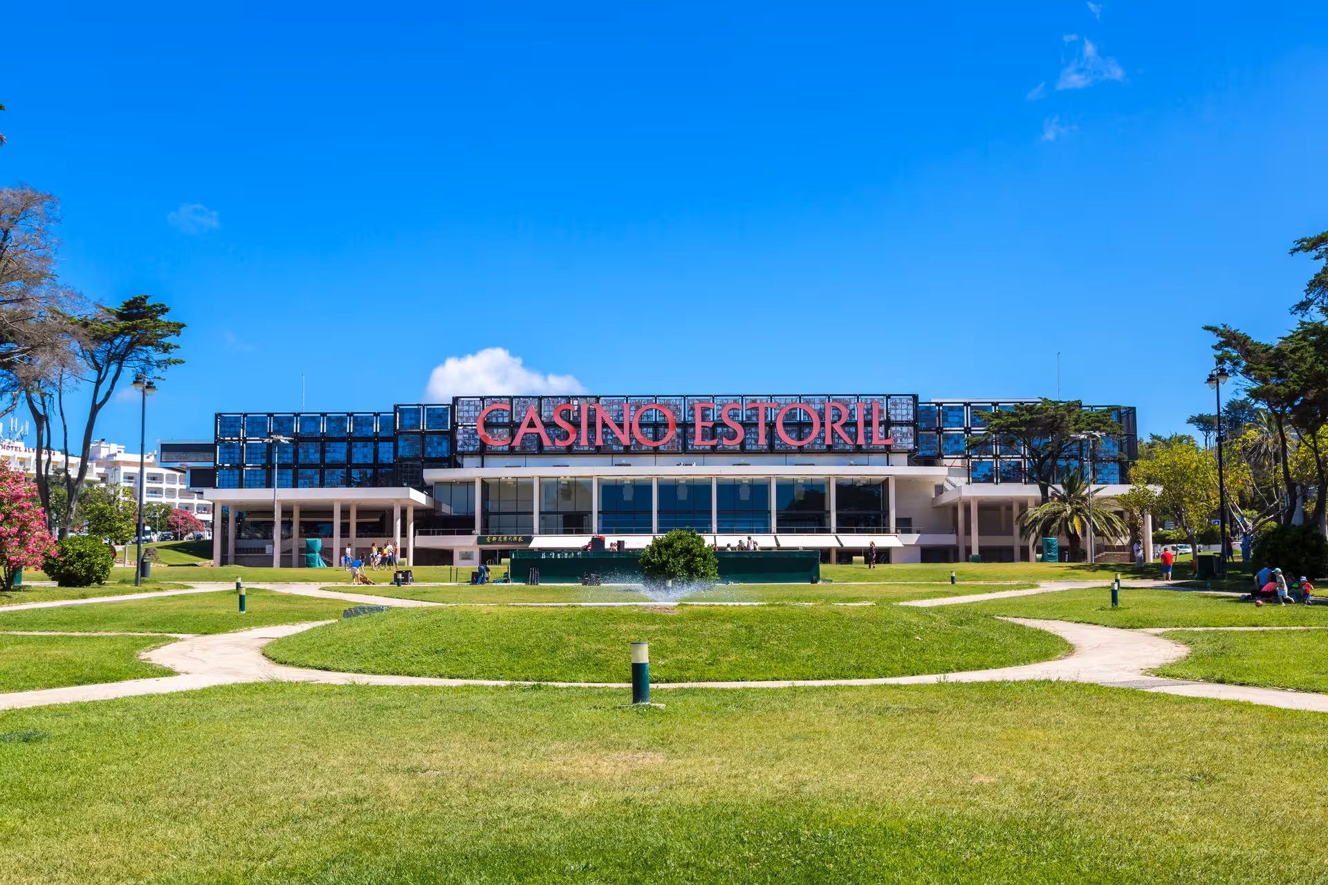 Front view of Casino Estoril surrounded by lush green gardens under a clear blue sky near Lisbon.