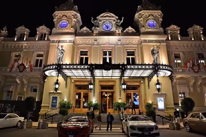 Casino de Monte-Carlo illuminated at night with luxury cars parked outside, Monaco