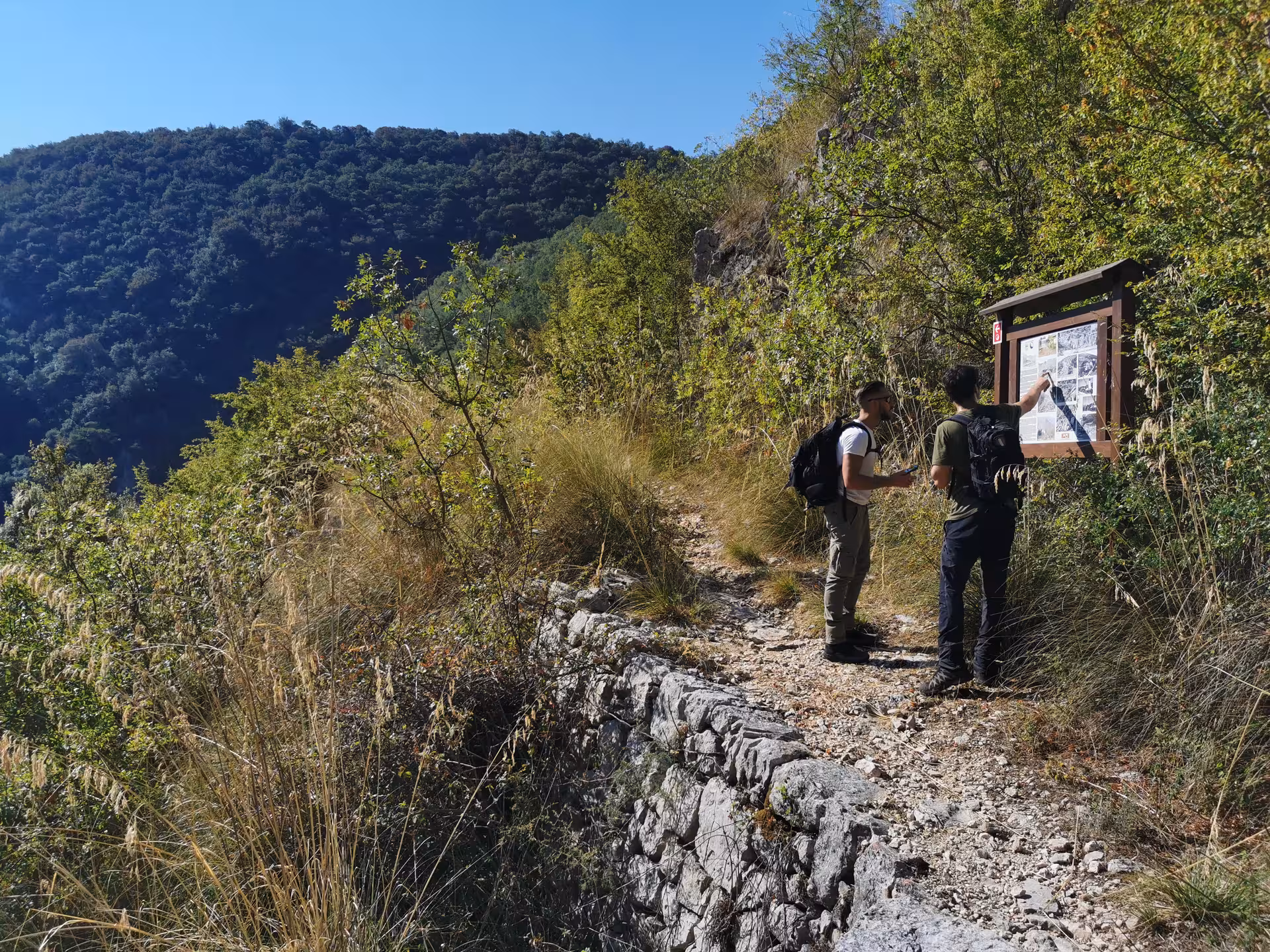 Two hikers studying a historical information board on a scenic trail during the Cassino Red Poppy walking experience.