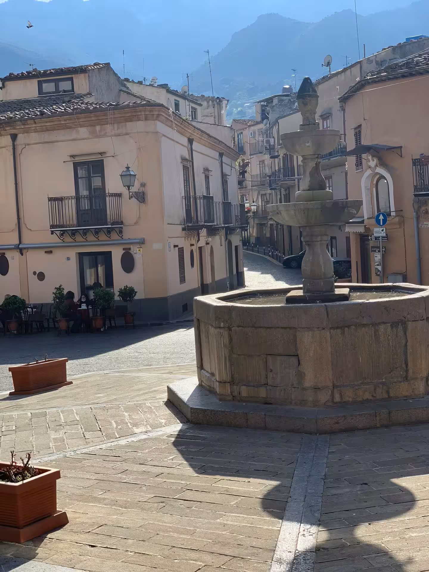 Quiet Castelbuono square with historic stone fountain, pastel houses and mountain views on private tour from Palermo