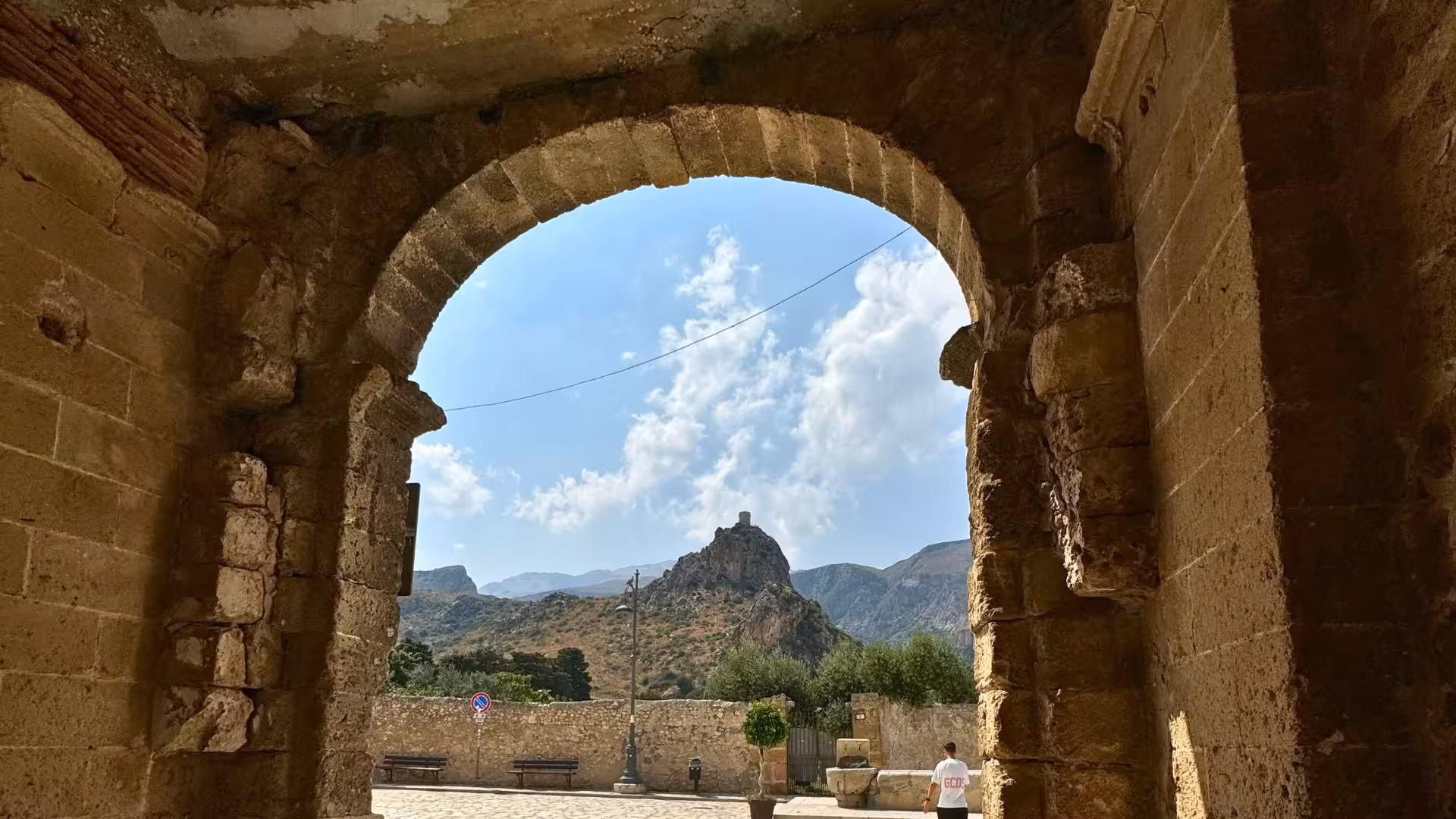 Historic stone archway frames a distant mountain view in Castellammare del Golfo.