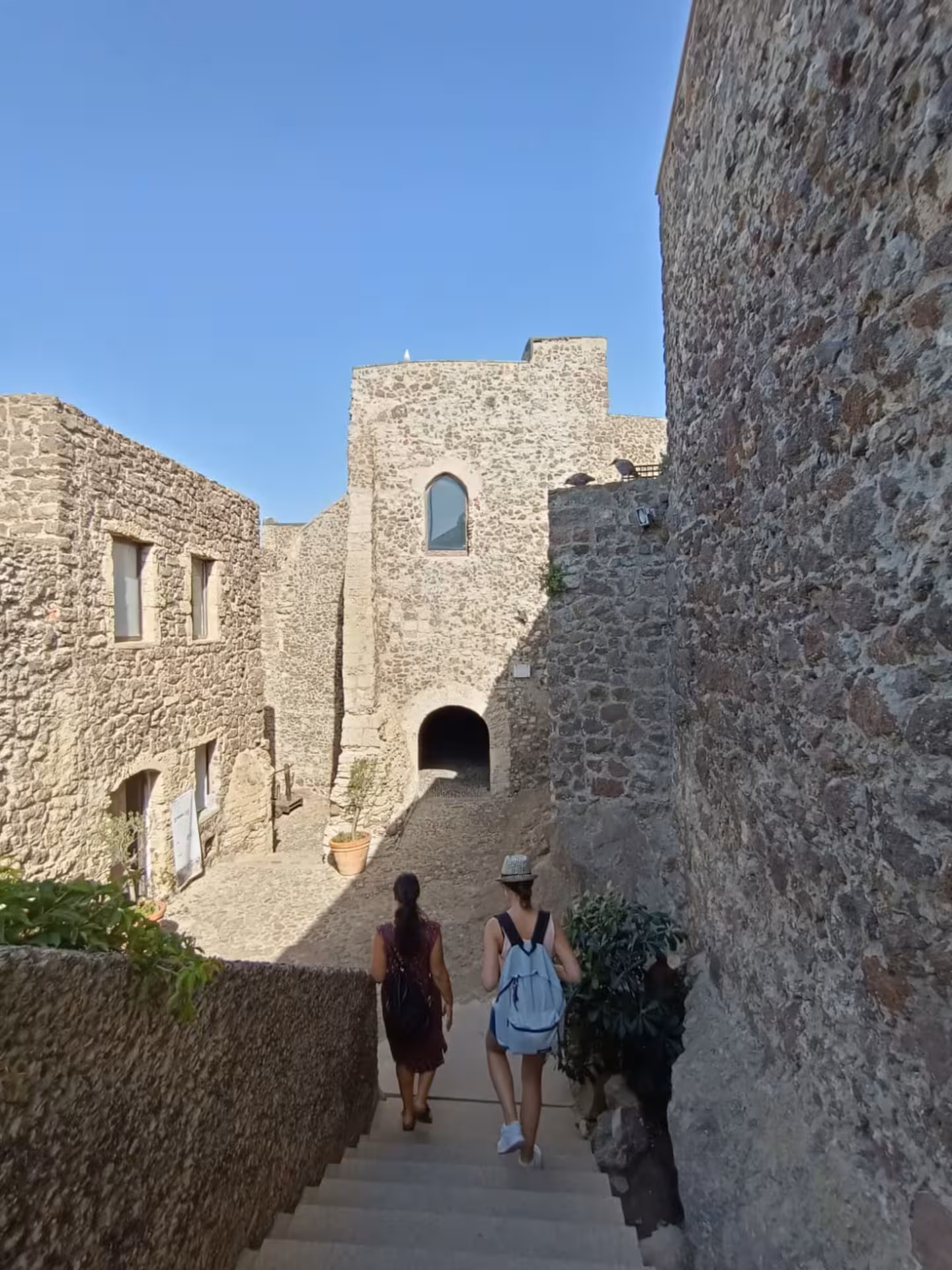 Tourists descend stone steps amidst ancient Castelsardo architecture on a sunny day.