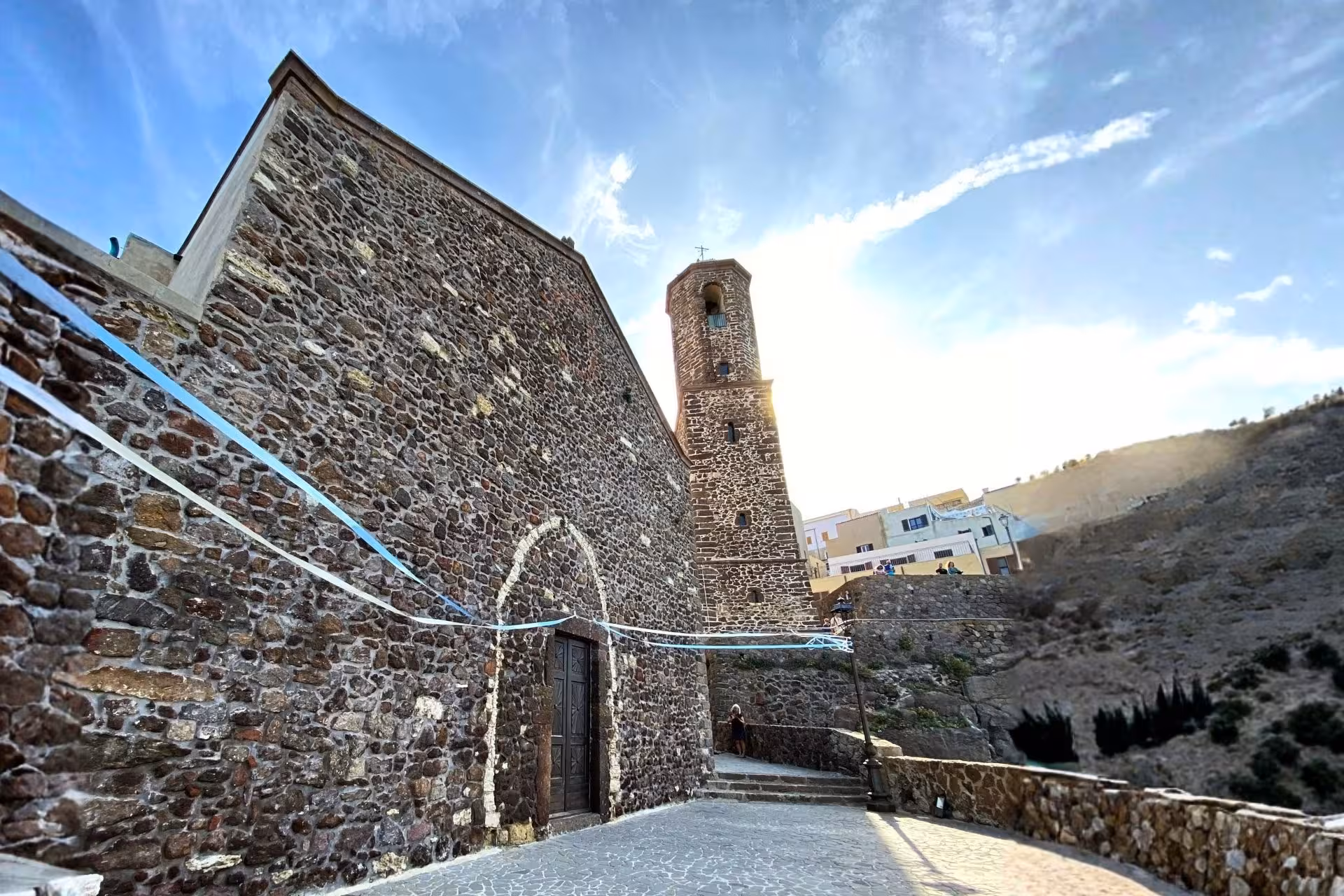 Historic stone church with bell tower in Castelsardo old town under a bright blue sky, perfect for cultural tours.