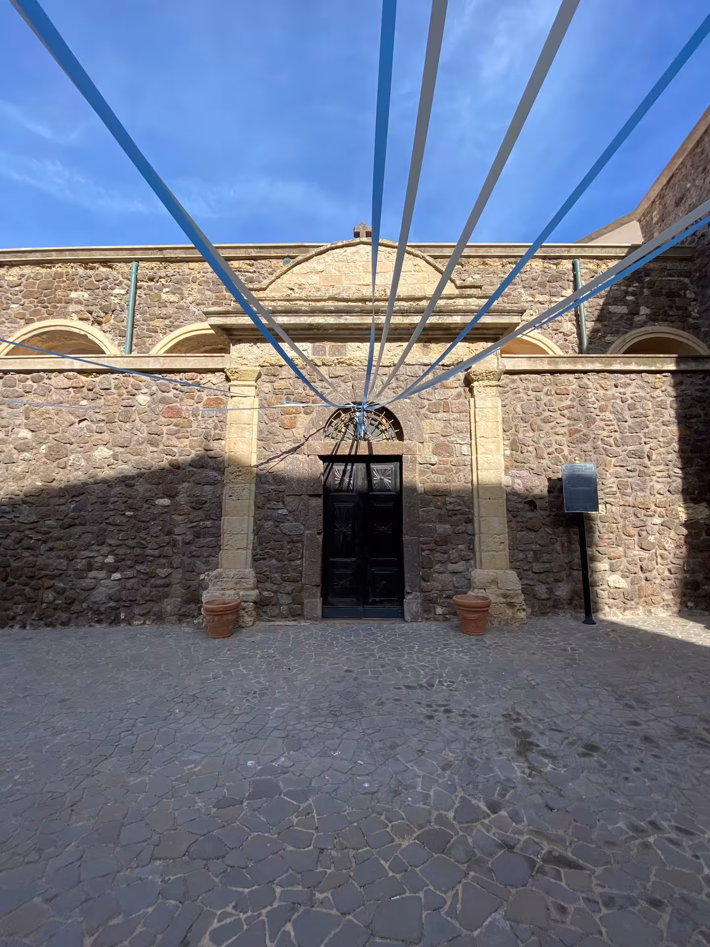 Entrance of Intreccio Museum in Castelsardo adorned with blue ribbons and rustic stone architecture.