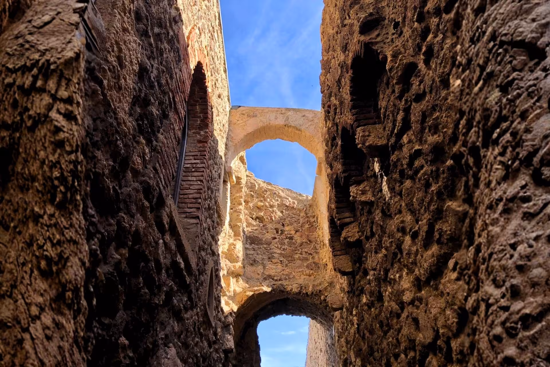 Ancient stone arches and narrow passageways in Castelsardo's old town, showcasing medieval architecture against a blue sky.