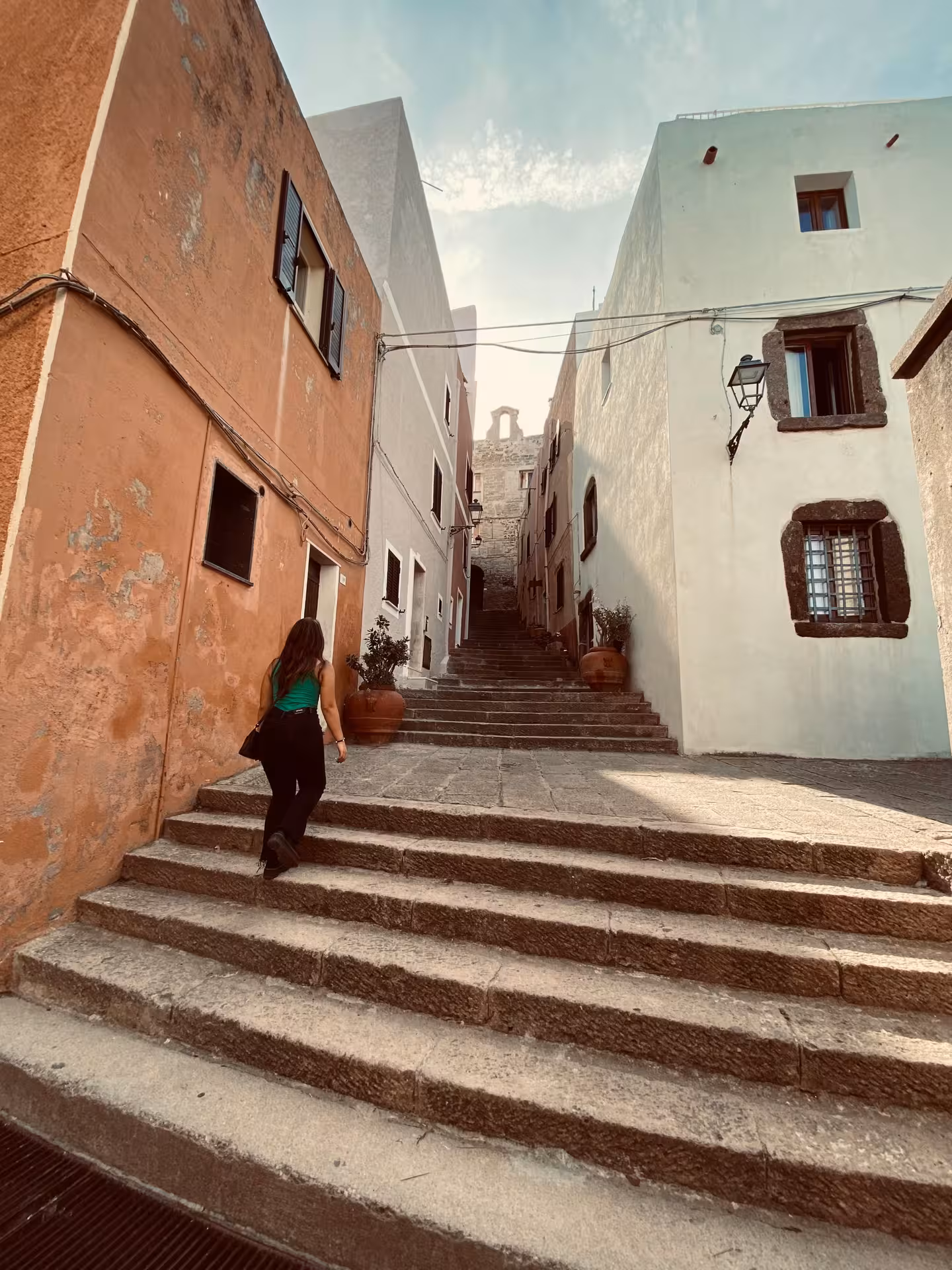 Woman walking up stone steps between colorful buildings in the charming streets of Castelsardo's old town.