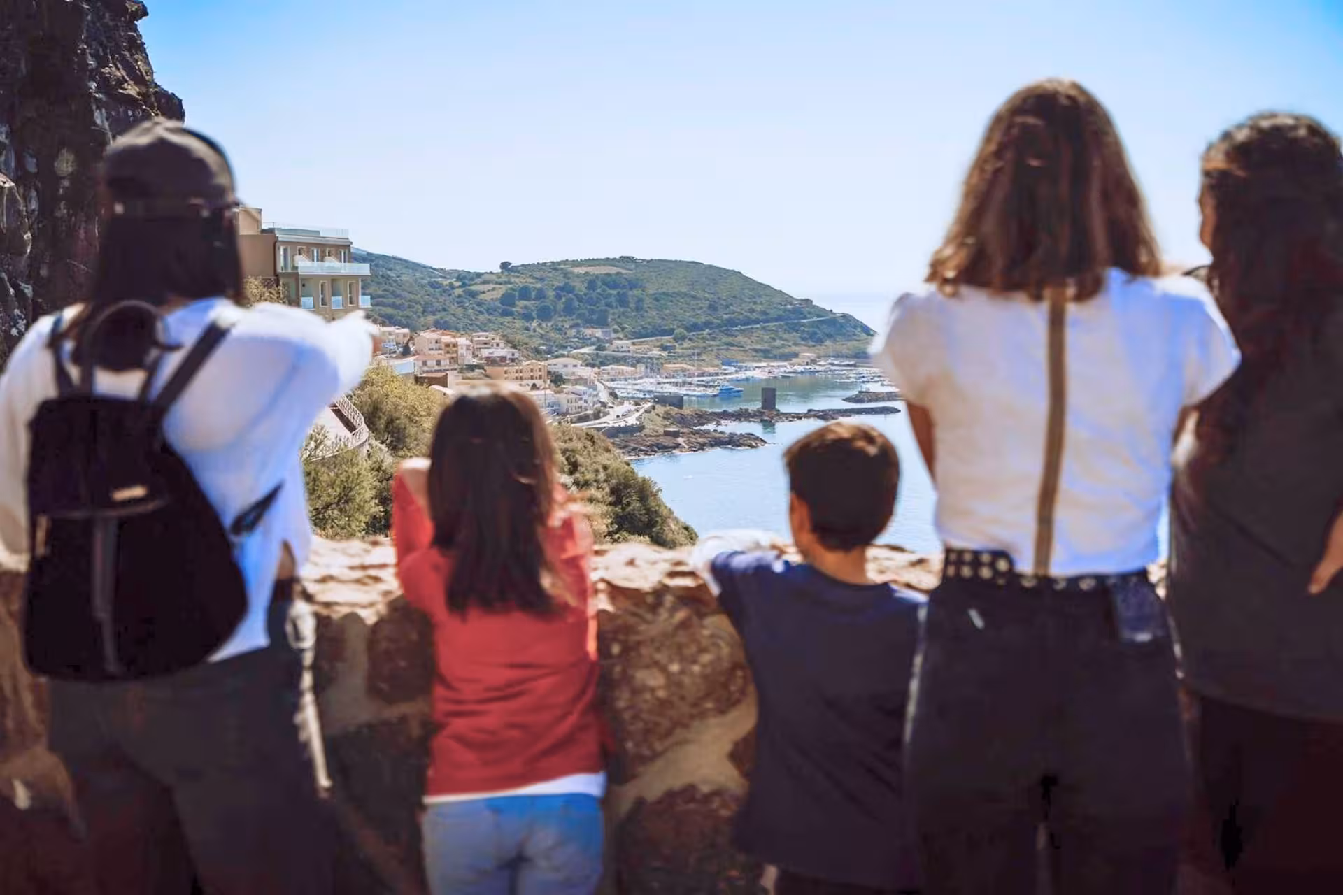 Group of tourists admiring panoramic view of Castelsardo's coastline and harbor under clear skies.