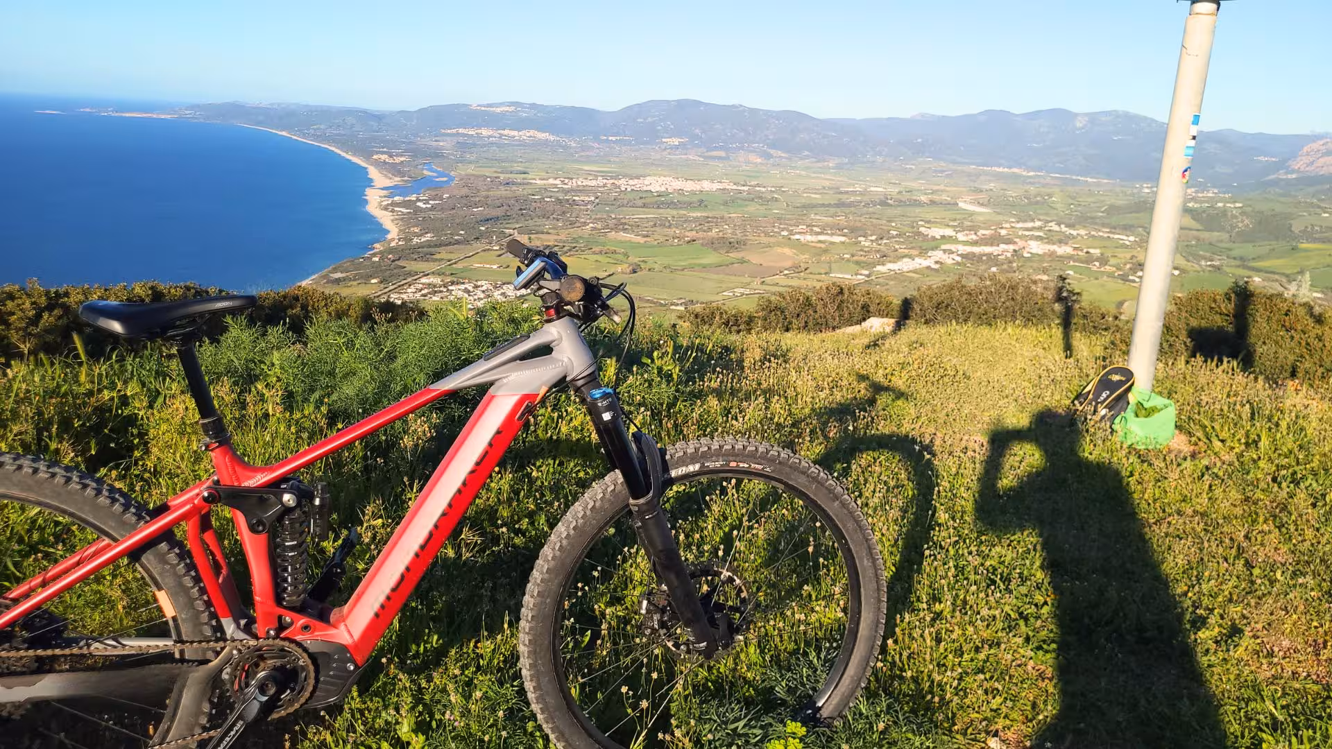 Scenic view of Castelsardo coastline with a red ebike on a grassy hill, perfect for panoramic tours.