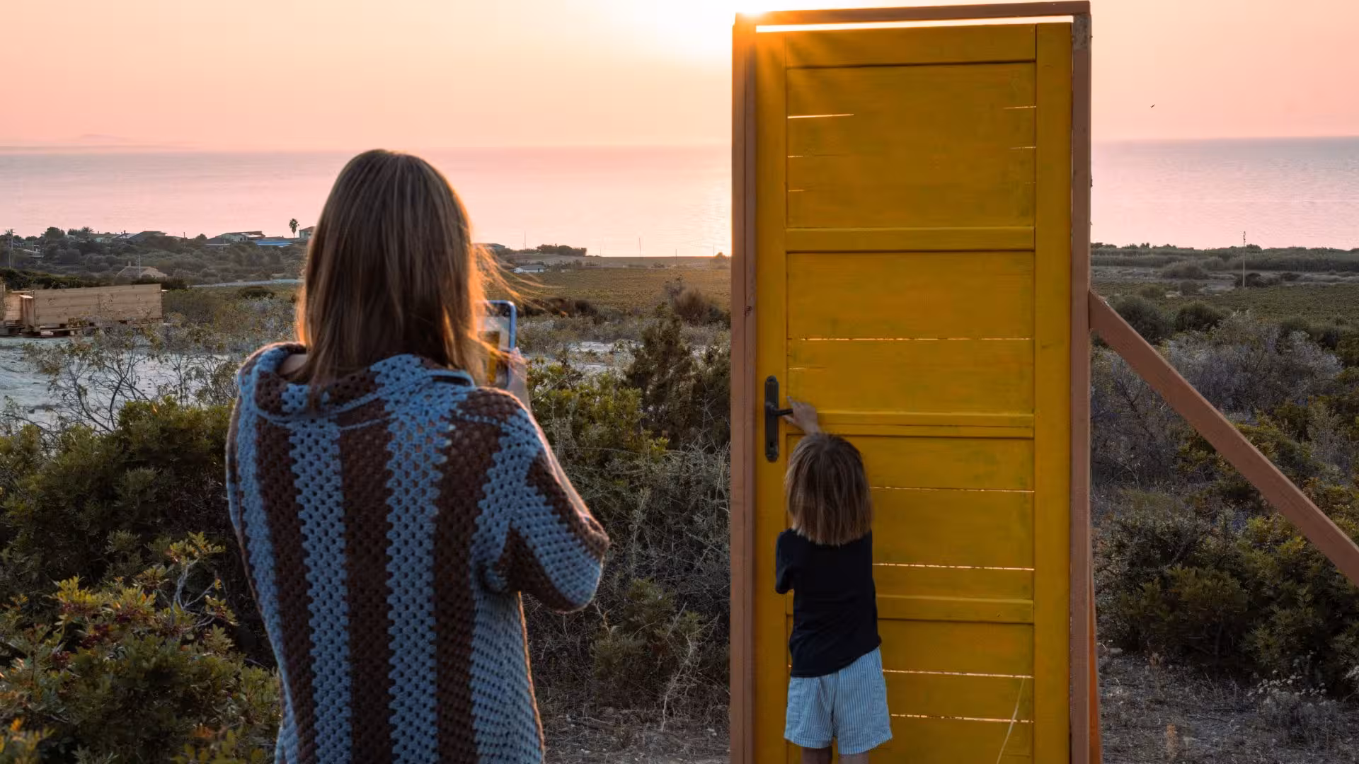 Woman and child enjoying sunset through a door frame, capturing the stunning Castelsardo coastal view.