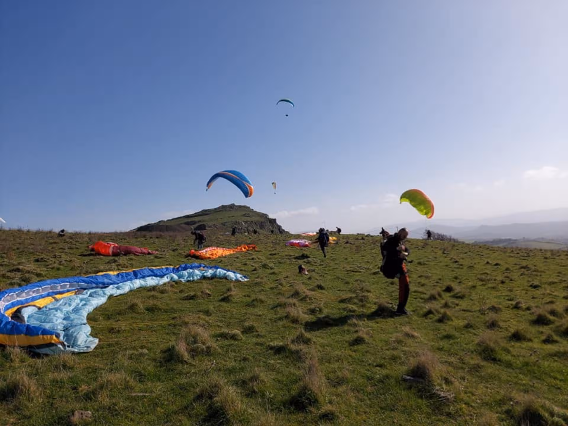 Paragliders readying for takeoff in Castelsardo, showcasing vibrant parachutes against a clear blue sky.