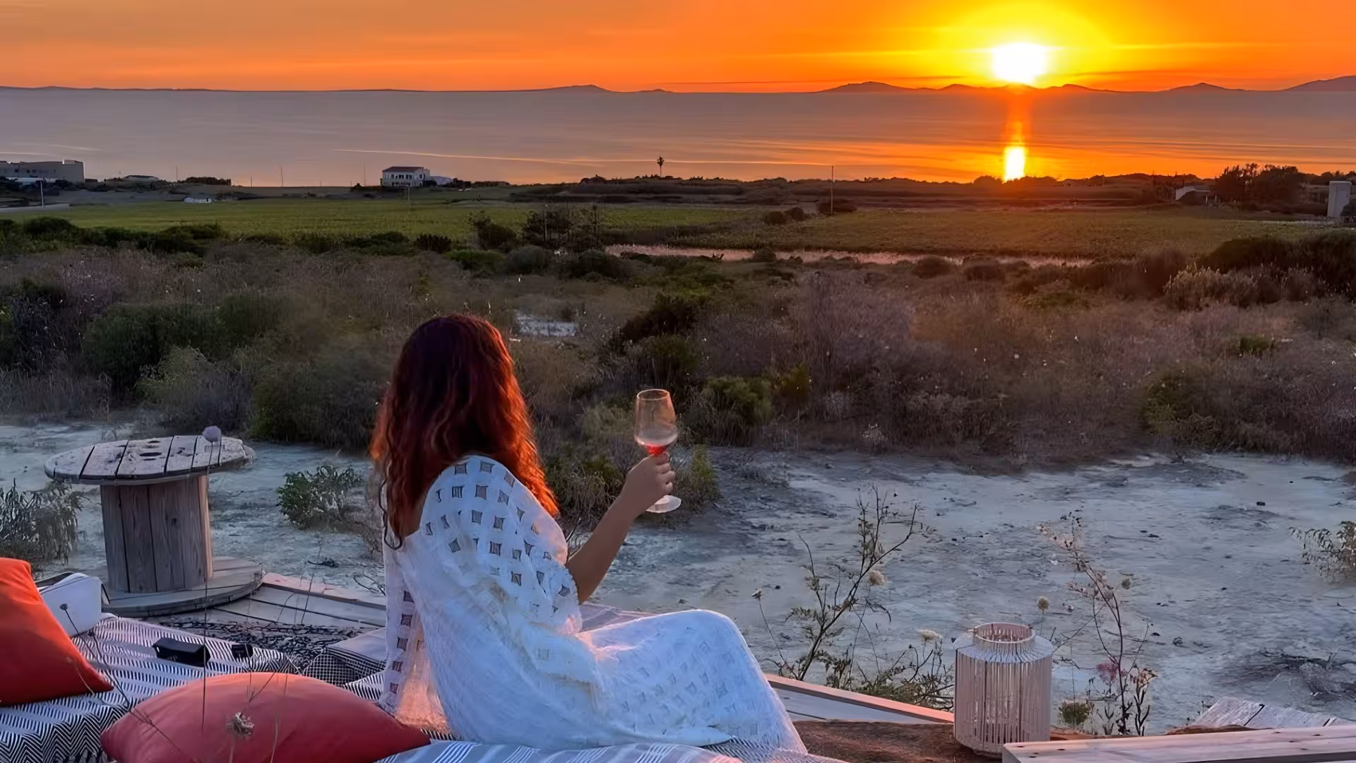 Woman enjoying wine at sunset in Castelsardo vineyard, overlooking scenic landscape and ocean view.