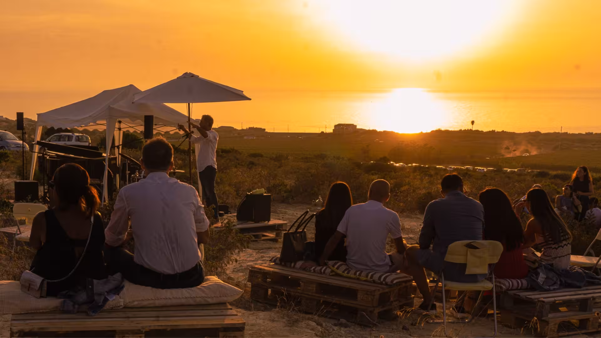 People enjoying a vineyard concert as the sun sets over Castelsardo's scenic landscape.