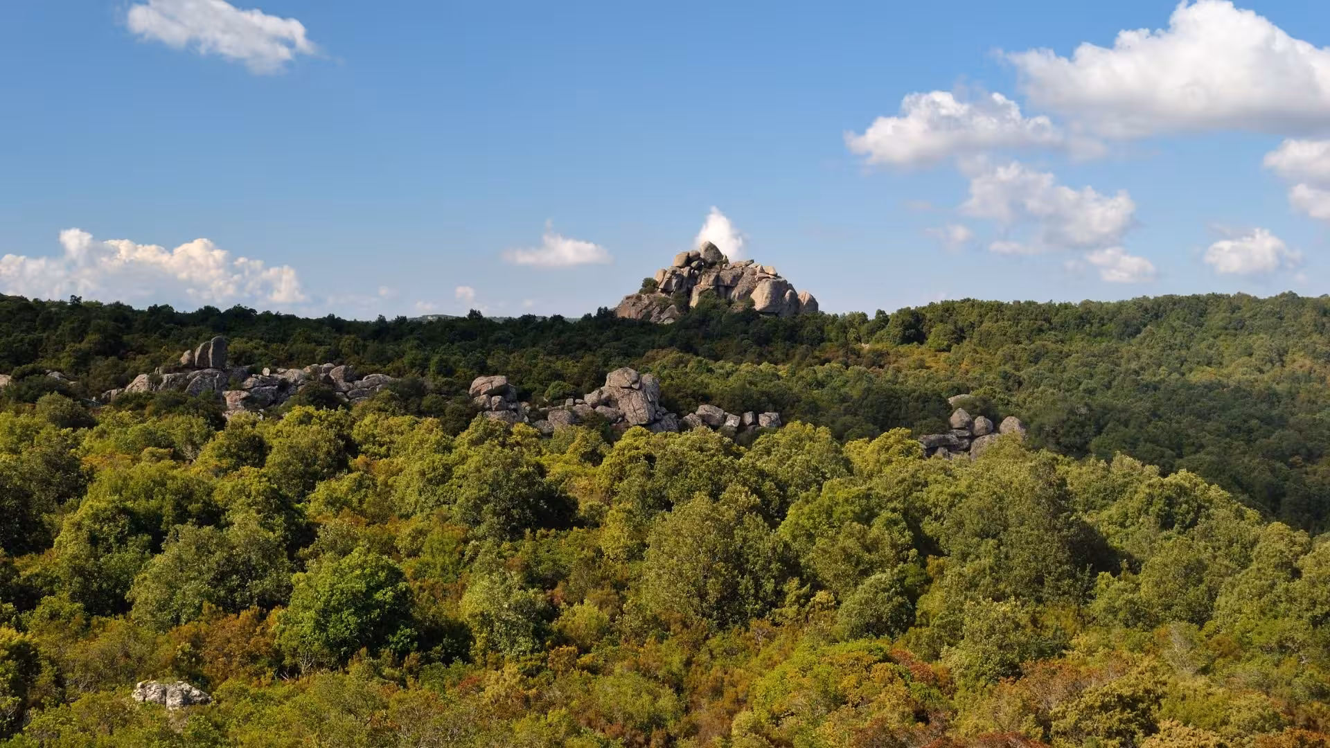 Scenic view of S'Acqua Callenti forest with rocky hilltops under a clear blue sky, perfect for trekking enthusiasts.