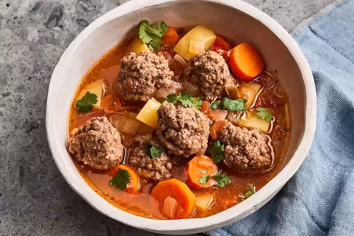 Hearty Catalan meatball soup with carrots and potatoes in a rich broth, ideal for an authentic Gràcia food experience.