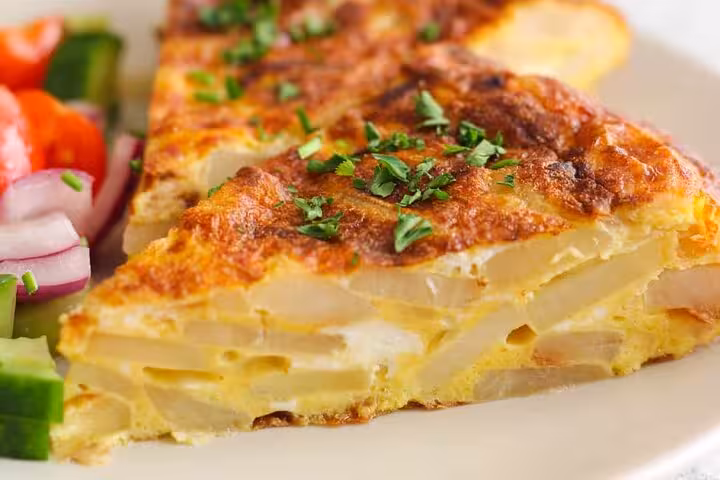 Savor authentic Catalan tortilla garnished with fresh herbs, a must-try on the Hidden Gràcia Food Tour in Barcelona.