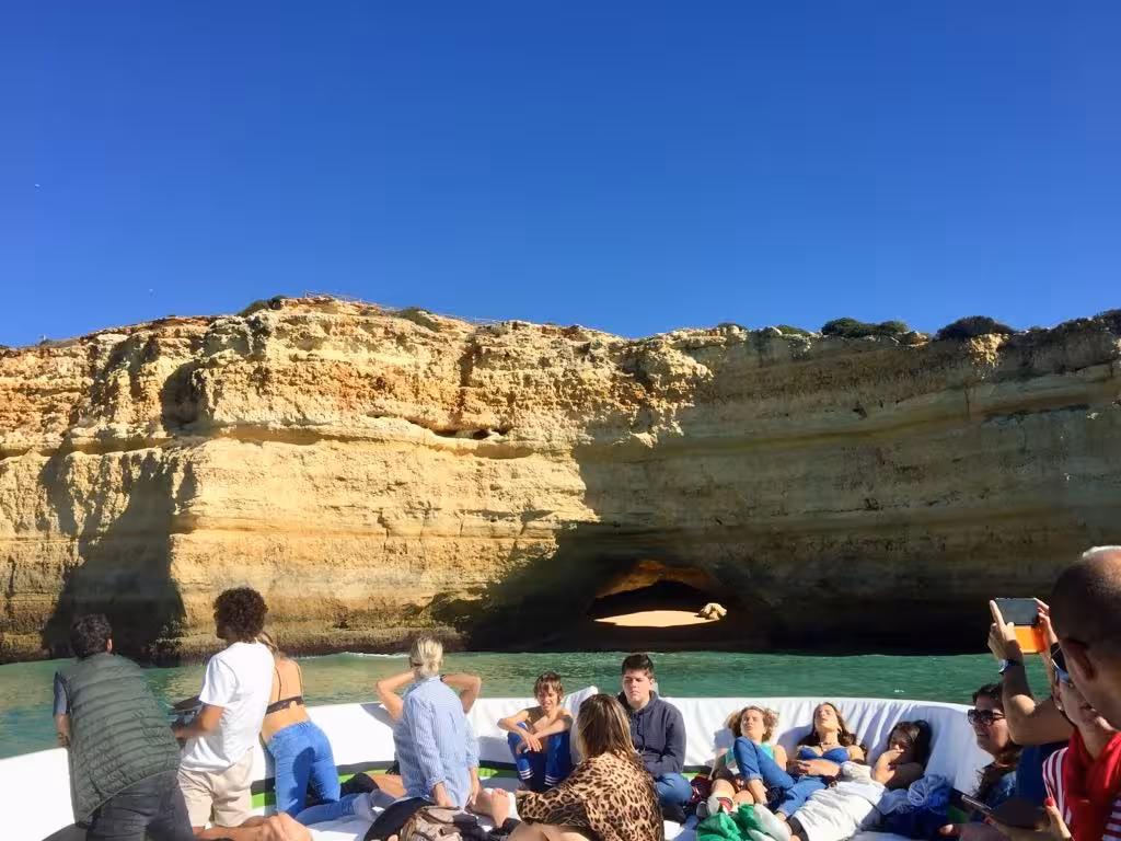 Relaxed group sunbathing on a catamaran in front of Benagil Cave’s sandy cove during a private Algarve coastline tour