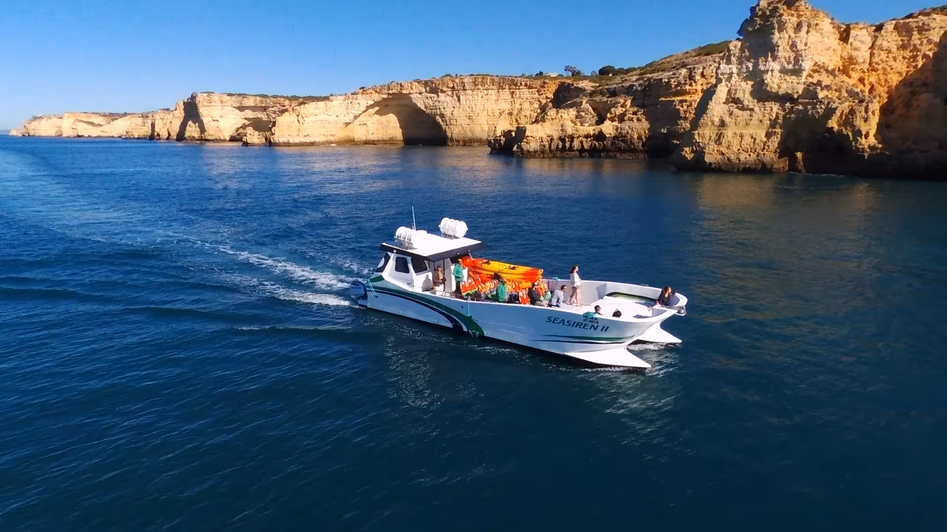 Modern catamaran cruising past Benagil and Marinha Beach cliffs on a private Algarve coast boat tour in clear blue sea