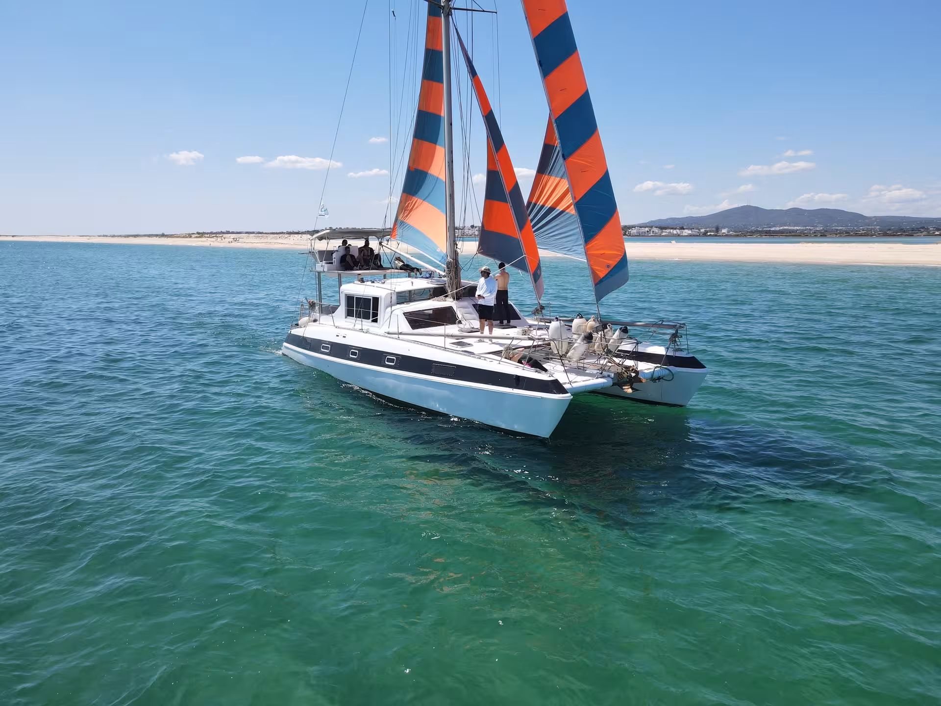 Catamaran sailing to the Blue Lagoon on a full-day cruise, guests on deck with orange-blue sails and clear sea