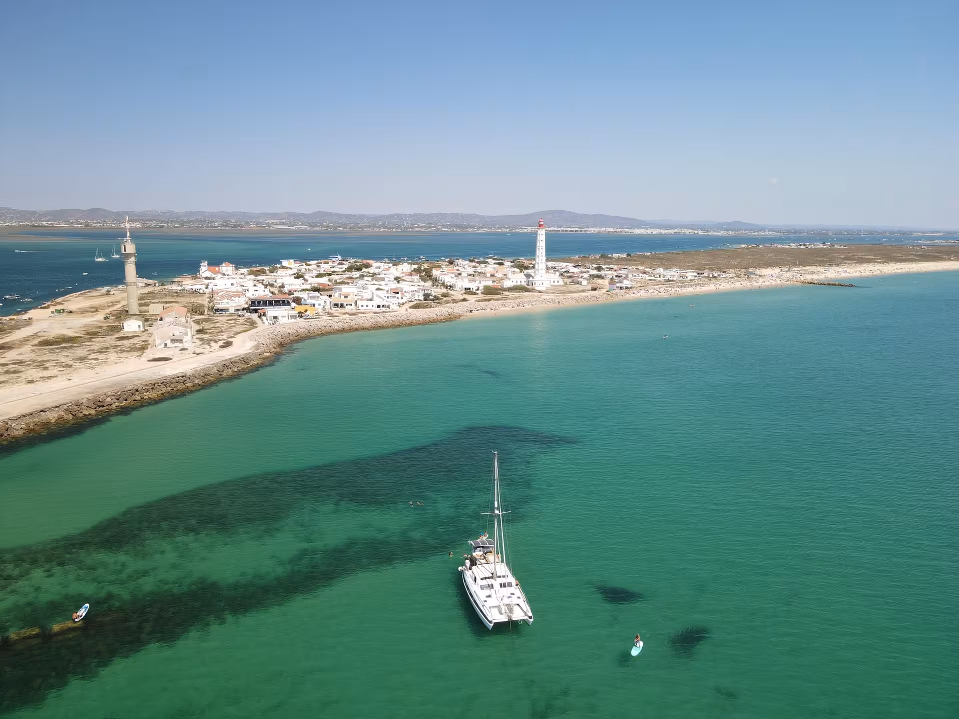 Catamaran anchored in turquoise Blue Lagoon near Faro lighthouse on full-day sailing and swim cruise