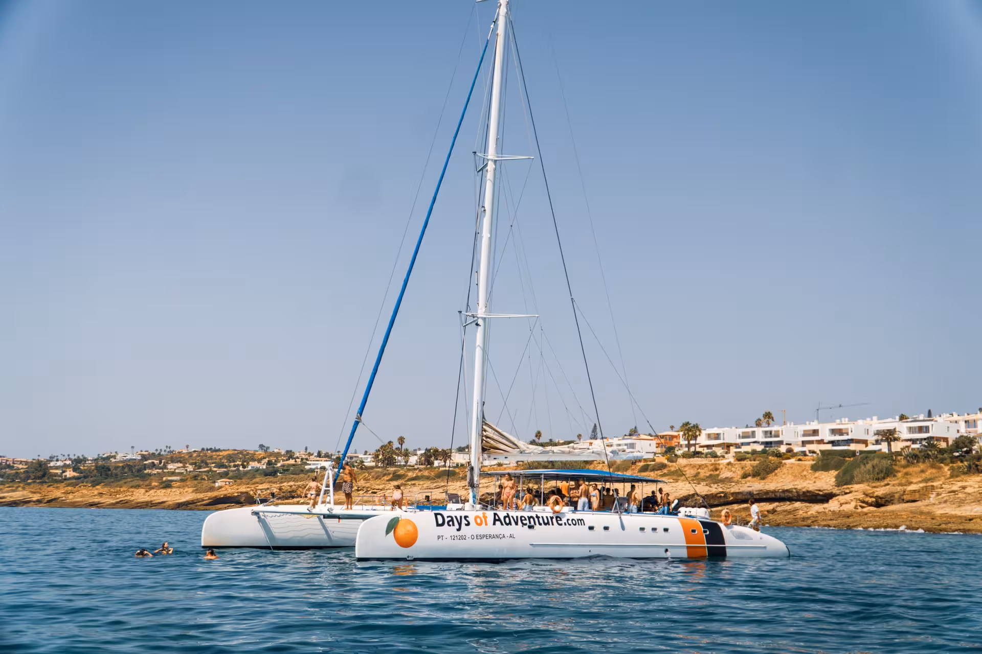 Days of Adventure catamaran anchored near Lagos coastline with guests swimming and enjoying a fun boat party tour.