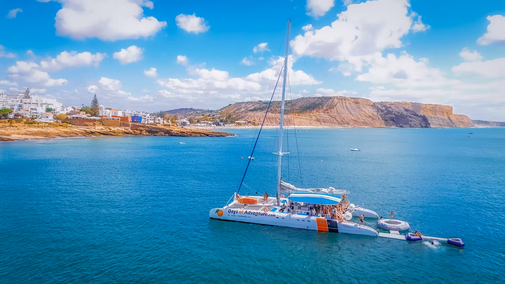 Aerial view of a catamaran anchored in turquoise Lagos waters with guests enjoying music and drinks on deck.