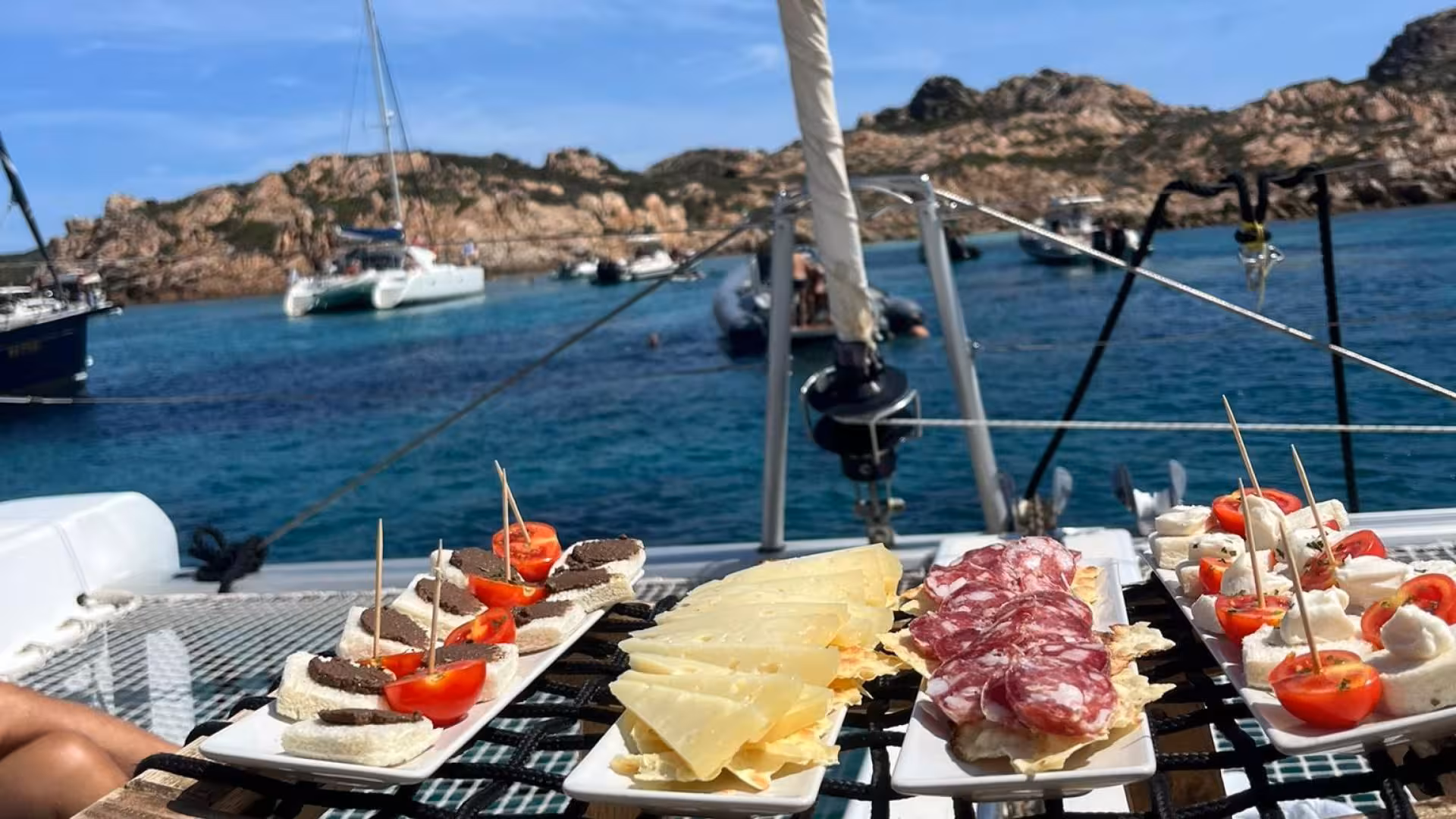 Gourmet appetizers on a catamaran with scenic views of La Maddalena Archipelago's crystal-clear waters.