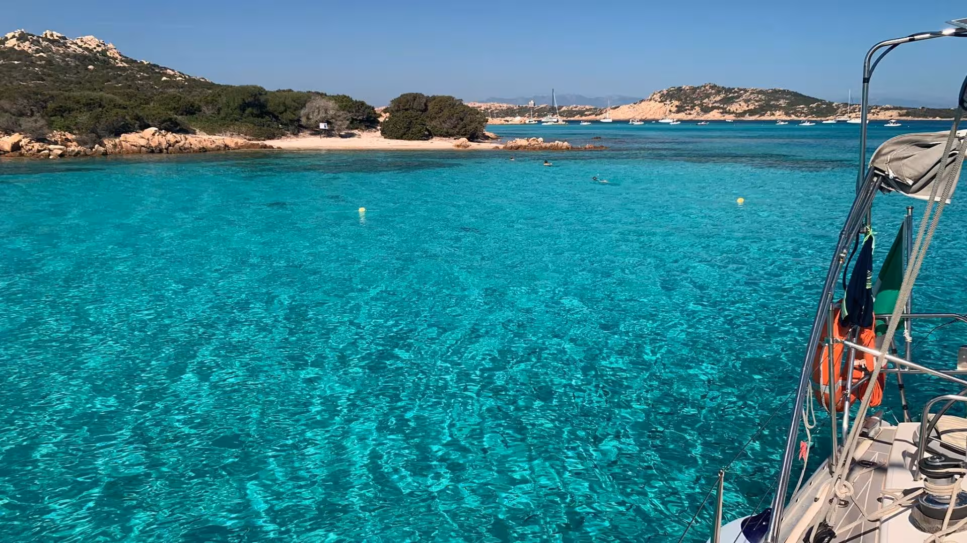 Crystal-clear turquoise waters and scenic coastline seen from a catamaran in the La Maddalena Archipelago.