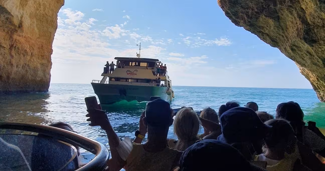 Catamaran Ophelia approaches a sea cave, capturing tourists' excitement and offering breathtaking views of the Algarve coast.