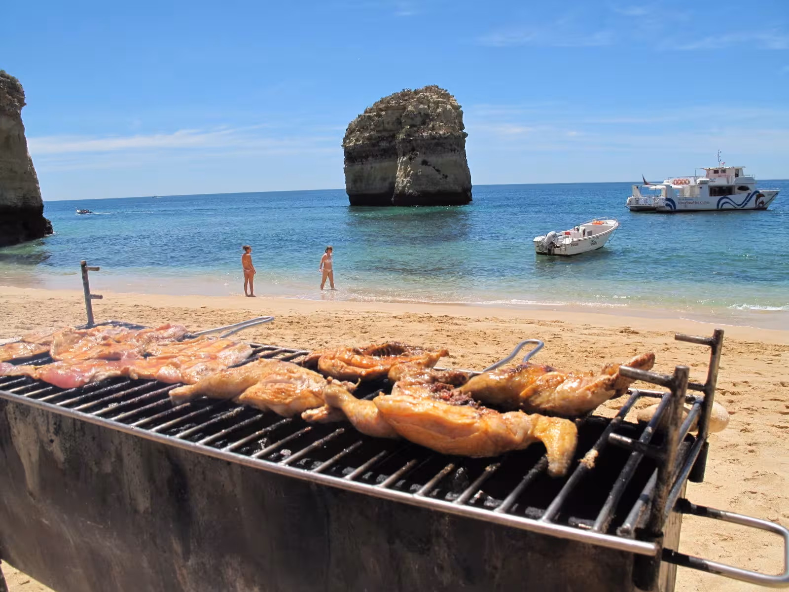 Grilled chicken sizzles on the beach BBQ with Catamaran Ophelia anchored nearby for the Benagil Caves tour.