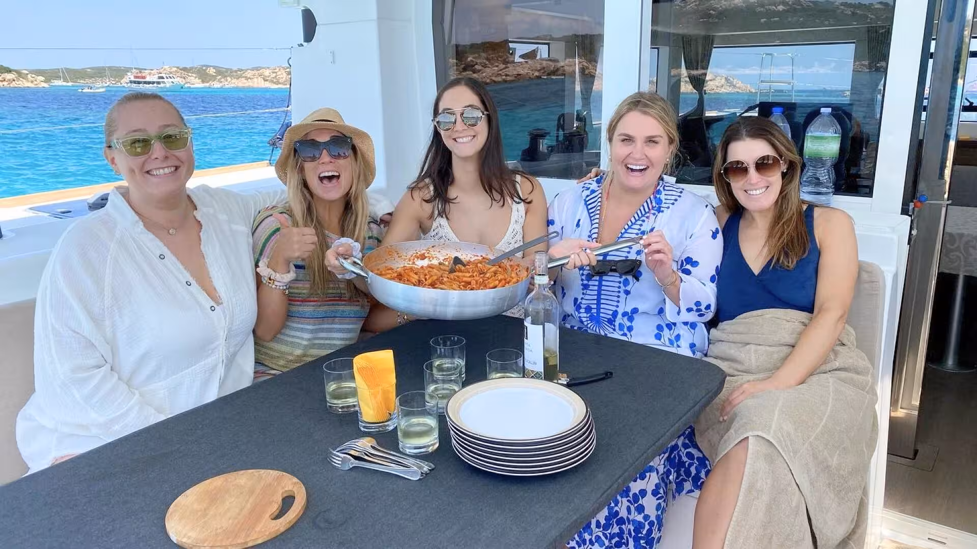 Group of friends enjoying a pasta meal aboard a catamaran in the scenic La Maddalena Archipelago.