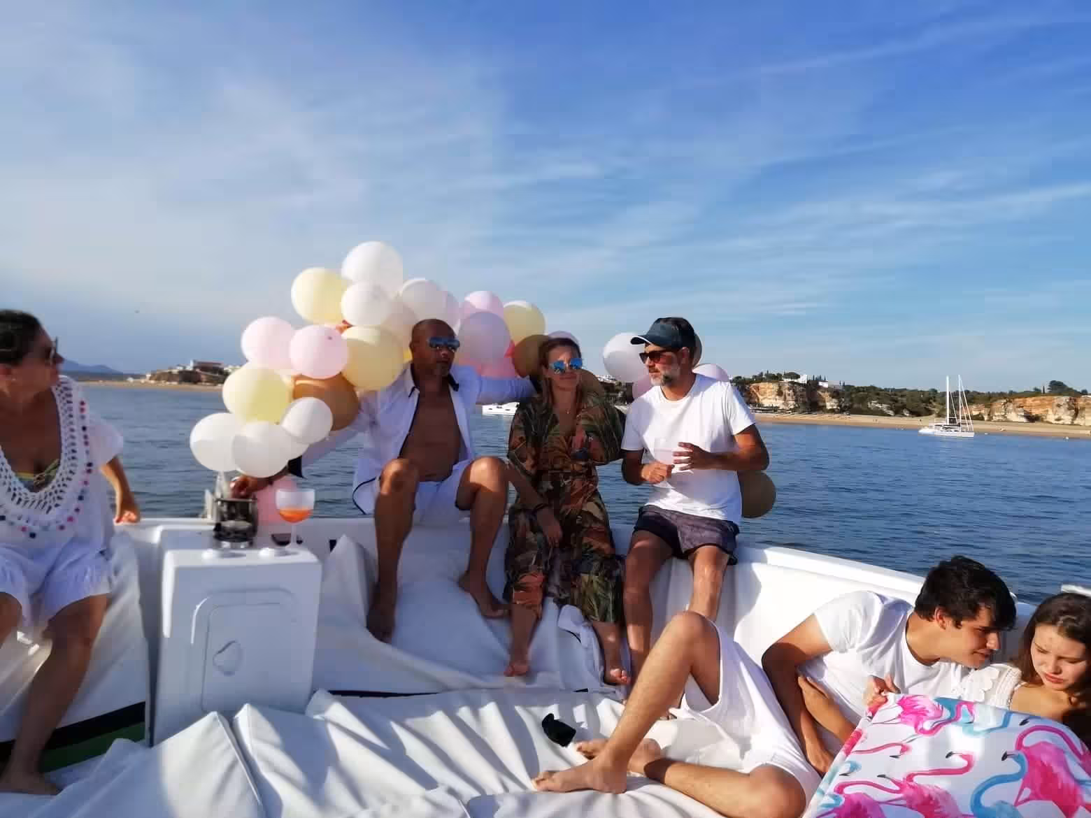 Friends celebrating on a private Algarve catamaran near Benagil and Marinha Beach, relaxing with drinks and balloons at sea