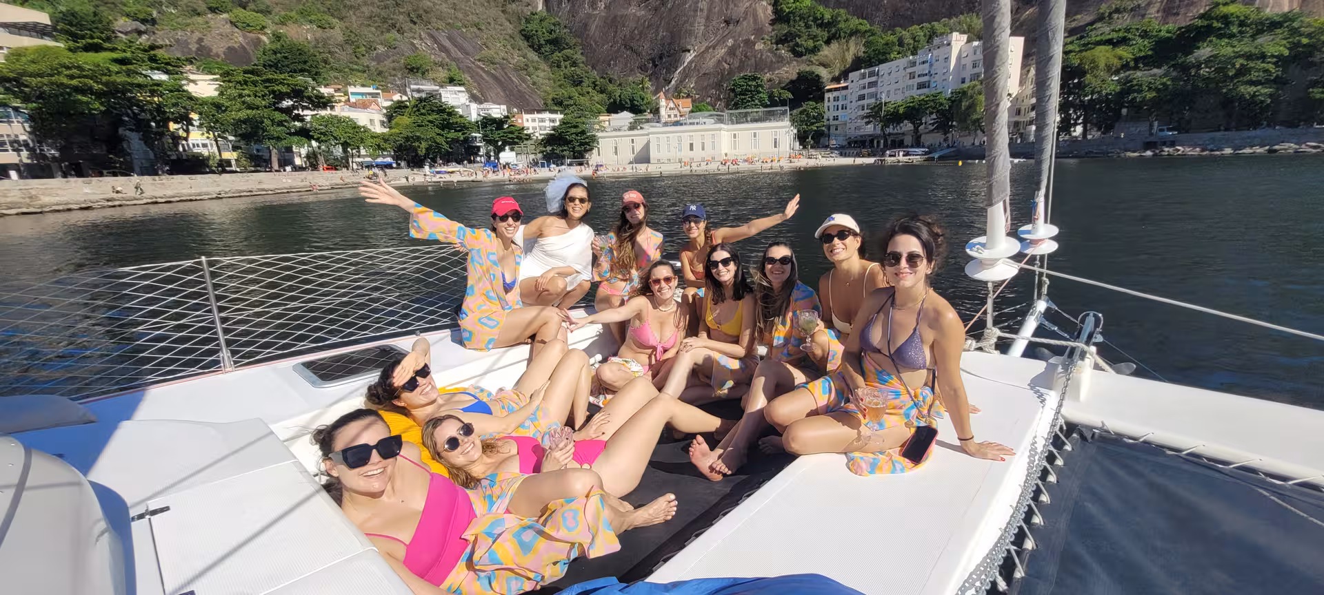 Friends relaxing on Velas do Rio shared catamaran tour in Rio de Janeiro bay with coastline views